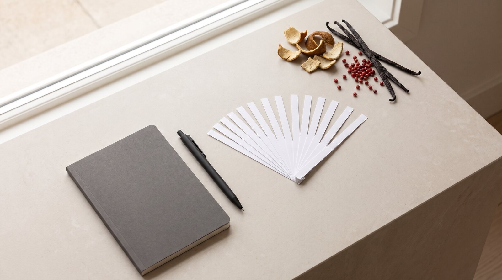 Helle Arbeitsfläche mit aufgefächerten Duftstreifen, Notizbuch, Stift und Rohstoffen